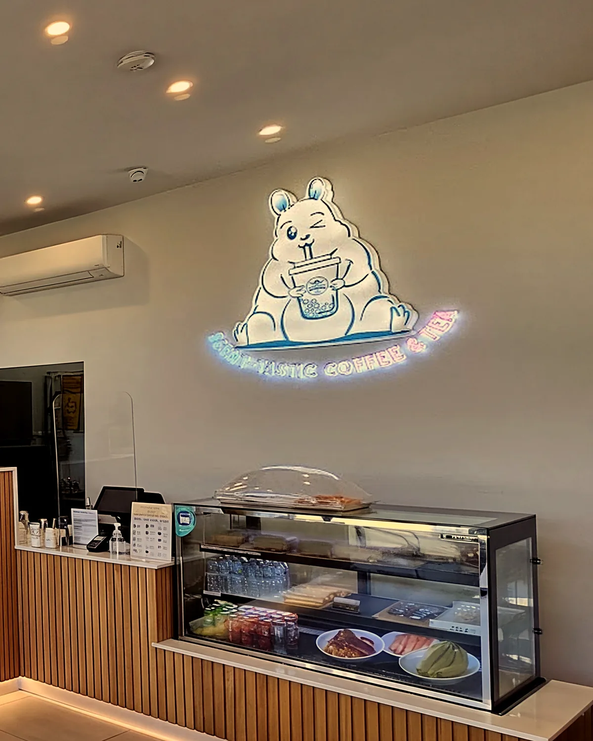 The neon squirrel holding a cup over their cake cabinet and timber counter